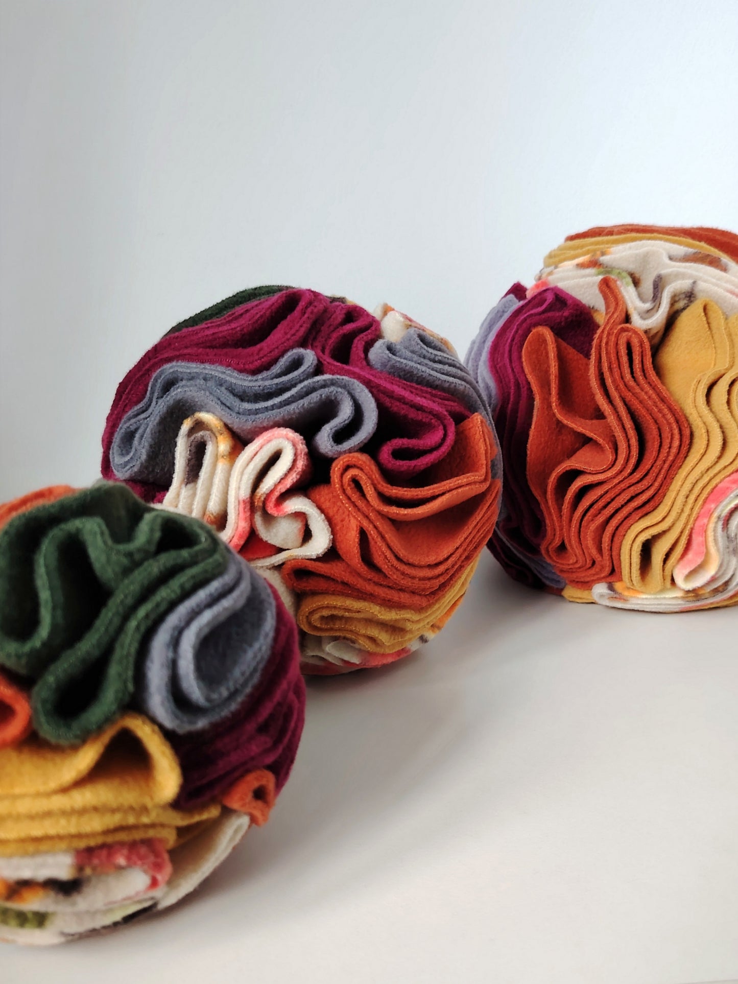 Three sizes of Autumn Snuffle Balls for dogs and small pets in rust, mustard, plum, green and grey fleece.