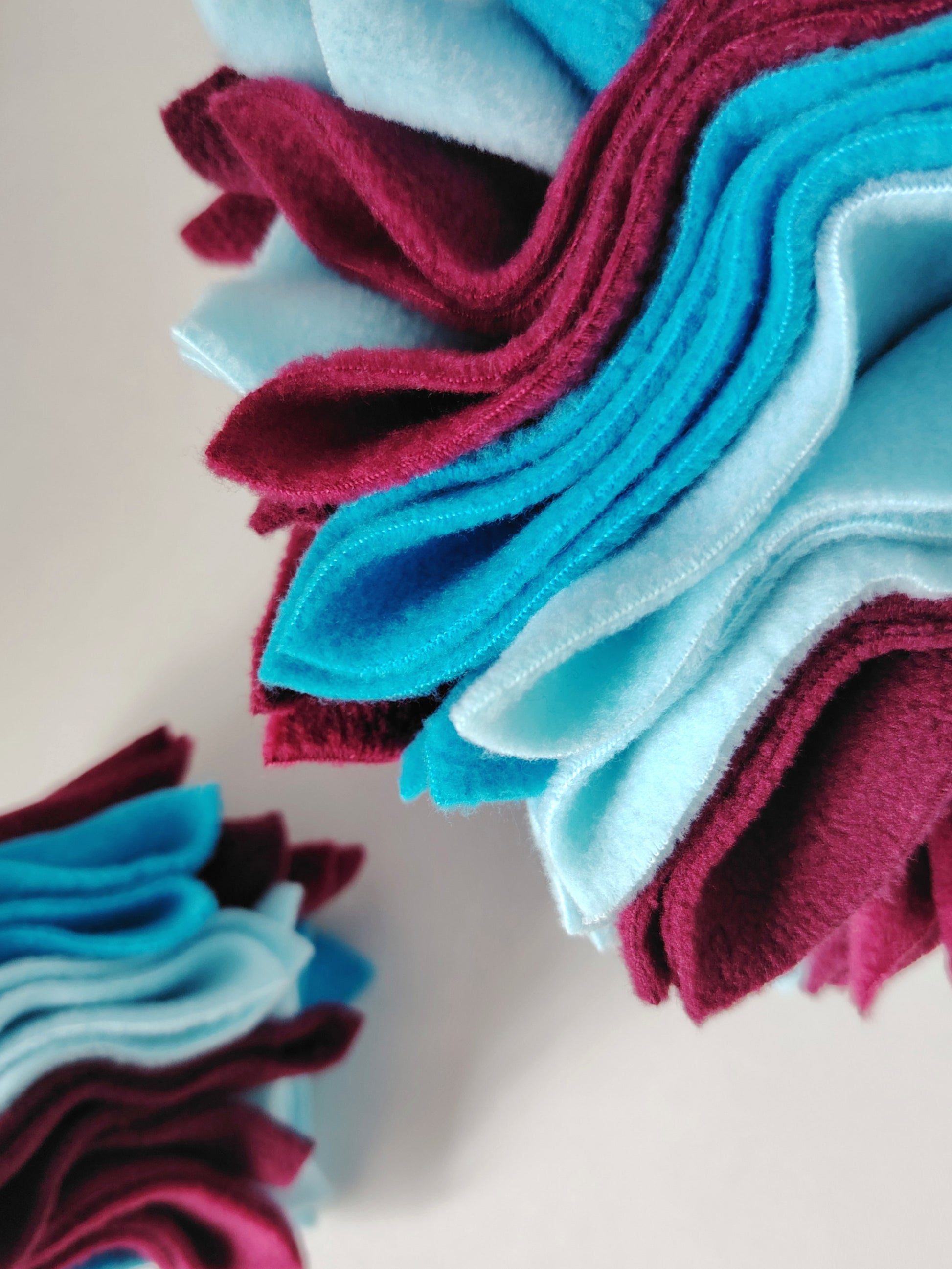 Close-up of a Nova Zeal Scruffle Ball showing layered turquoise, light blue and burgundy fleece folds.