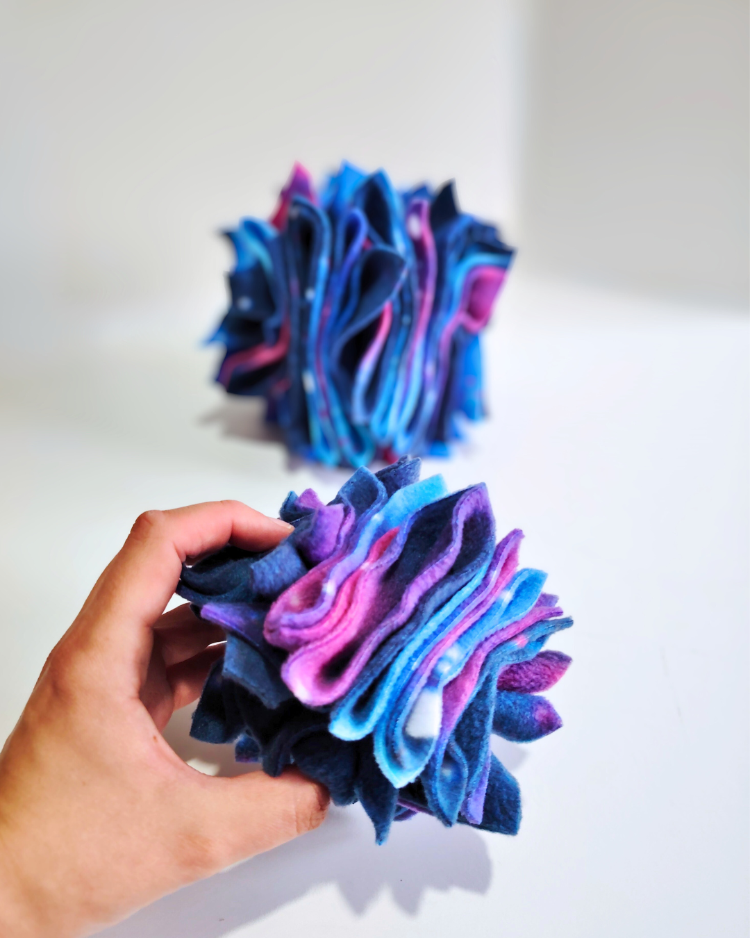 Hand holding a small enrichment toy with the large version sitting behind against a white background