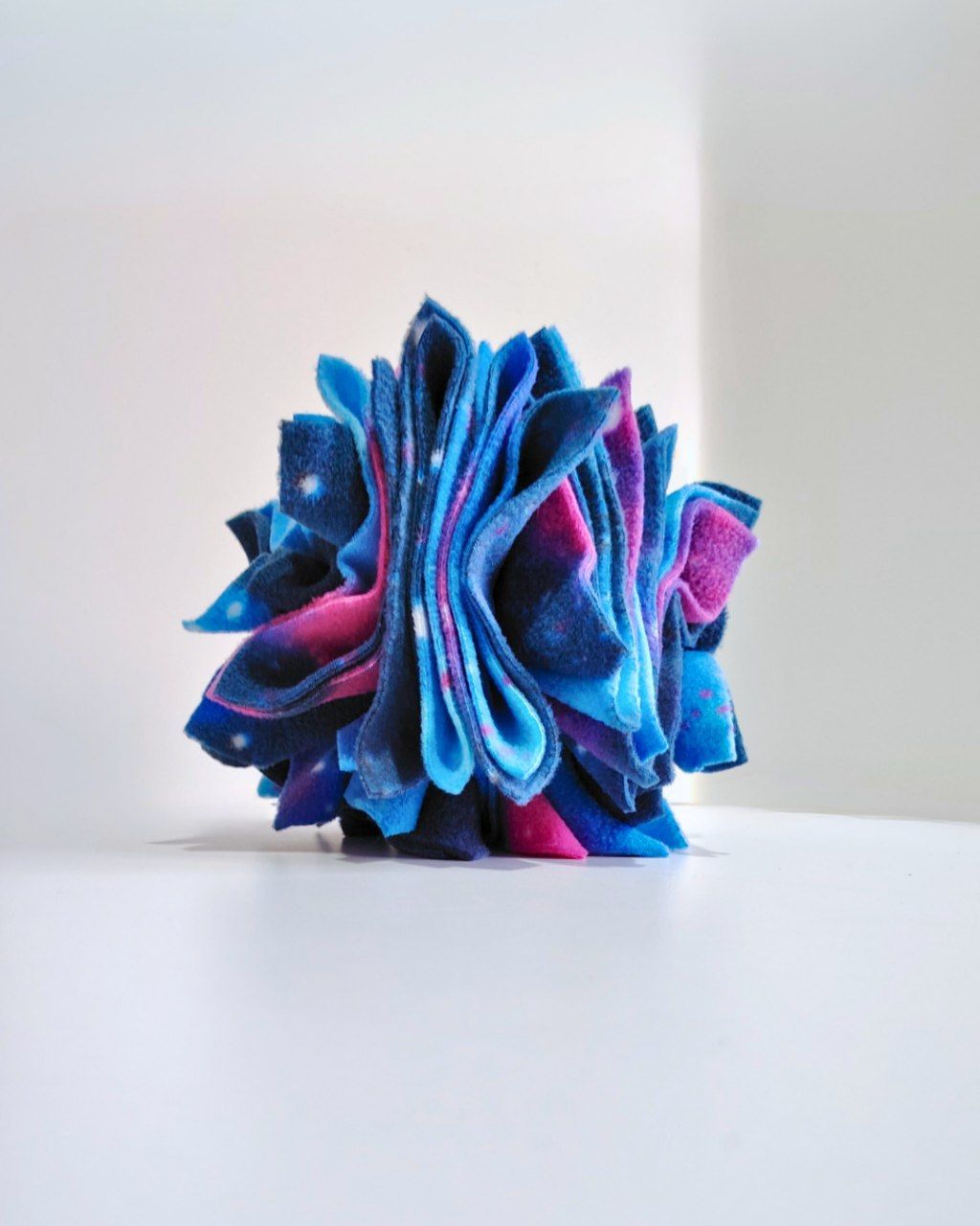 Blue and pink galaxy fleece folded to represent a Star on a white surface with a light gray background