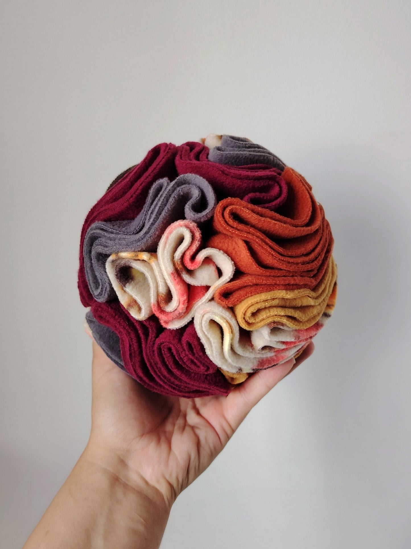 Medium Autumn Snuffle Ball for dogs and small pets in one hand to show its size and fleece folds.