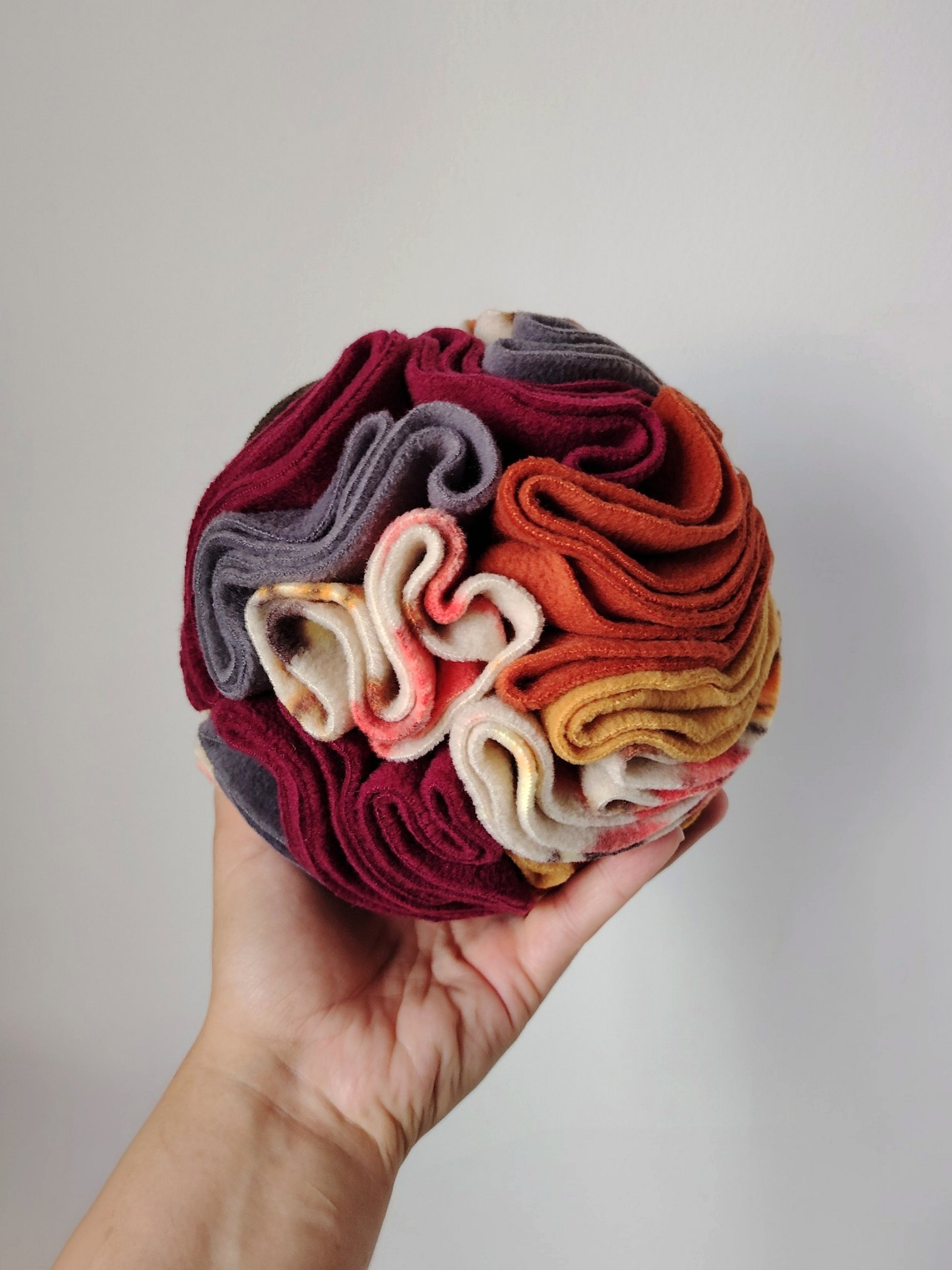 Medium Autumn Snuffle Ball for dogs and small pets in one hand to show its size and fleece folds.