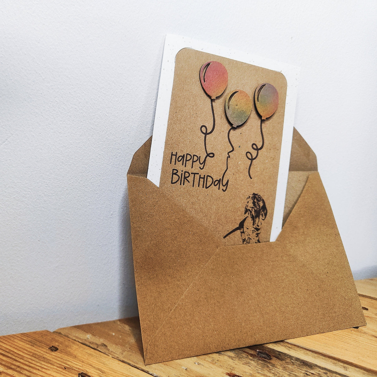Miniature Dachshund birthday card with colourful raised balloons shown standing inside a kraft envelope.