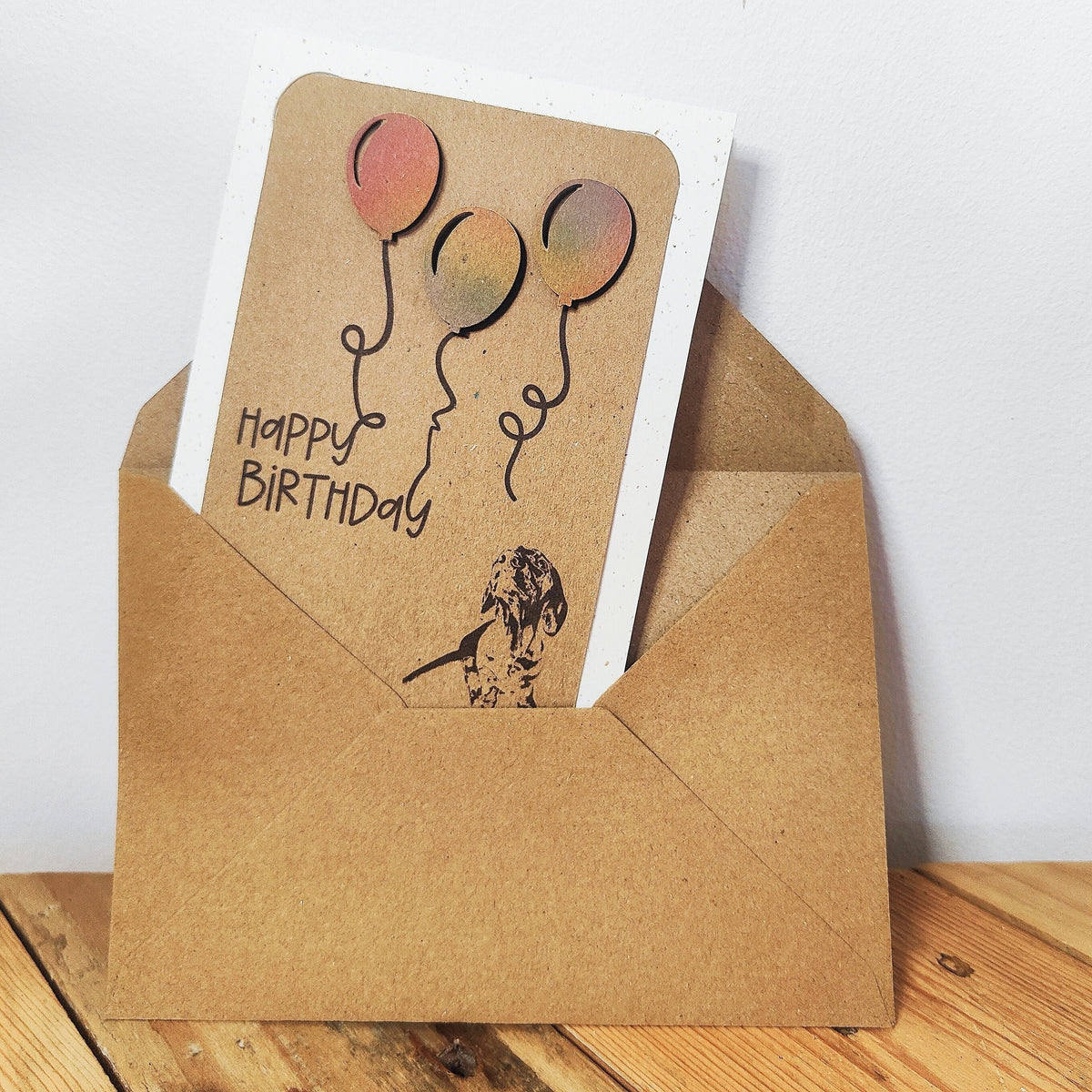 Miniature Dachshund birthday card with colourful balloons shown inside a kraft envelope.