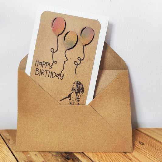 Miniature Dachshund birthday card with colourful balloons shown inside a kraft envelope.