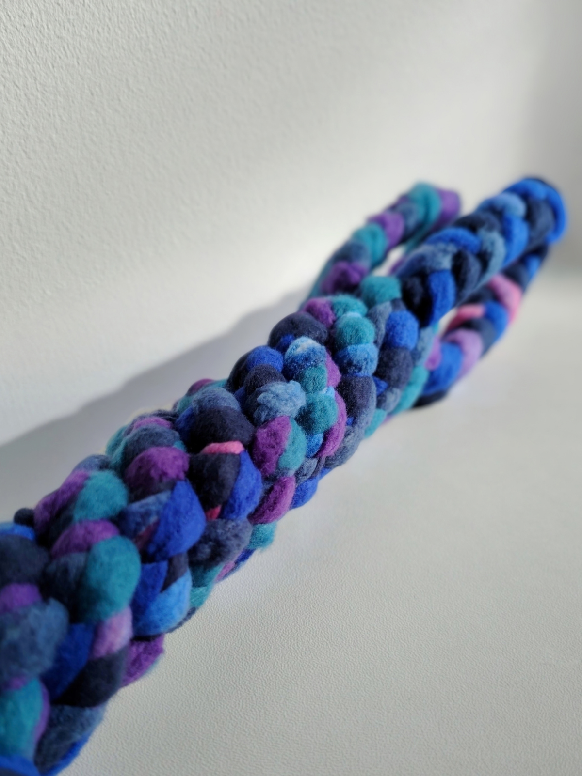 Close-up of the braided fleece construction of a handmade Nova Zeal Night Sky tug toy, showing interwoven navy, royal blue, teal and purple fleece against a light background.