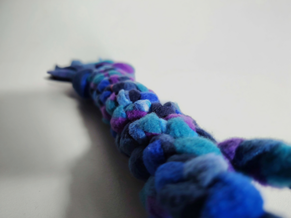 Low-angle close-up looking along a handmade Nova Zeal Night Sky fleece tug toy, showing braided navy, royal blue, teal and purple fleece with a softly blurred foreground and background.