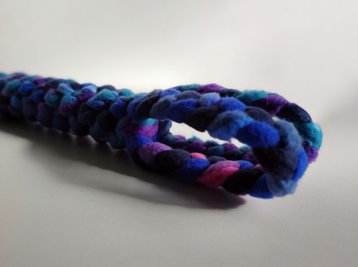 Close-up of the braided loop handle of a handmade Nova Zeal Night Sky fleece tug toy, featuring navy, royal blue, teal and purple against a light background.