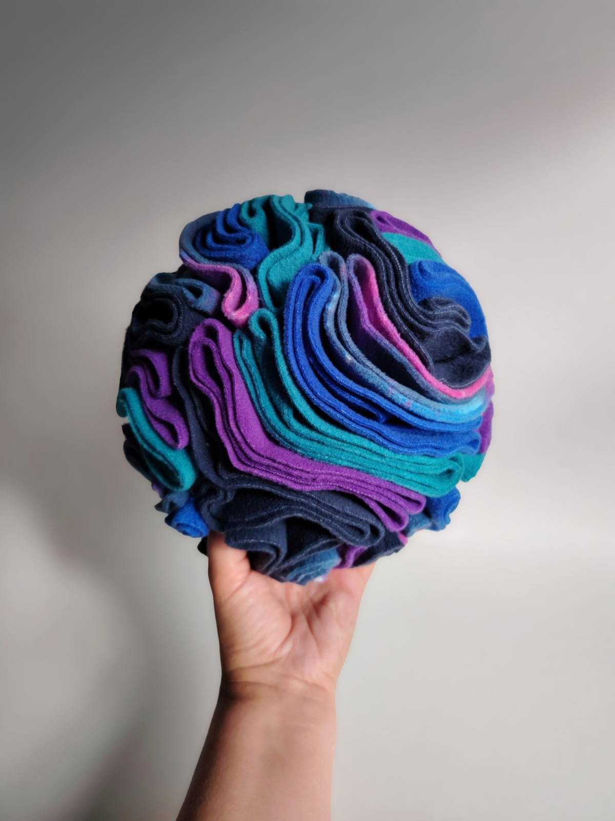 Large Nova Zeal Night Sky Snuffle Ball held in one hand to show its size, featuring densely folded fleece in navy, royal blue, teal, purple and galaxy print.