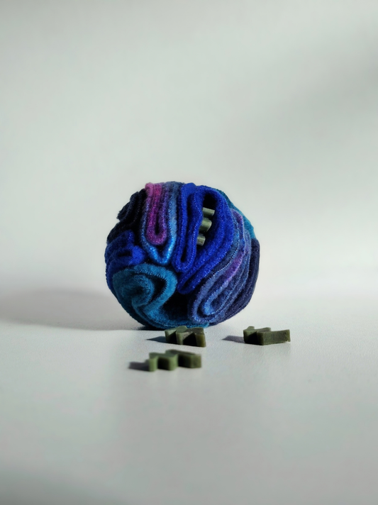 Nova Zeal Night Sky Pocket Snuffle Ball in navy, royal blue, teal and purple fleece, displayed with small green dog treats on a white background.