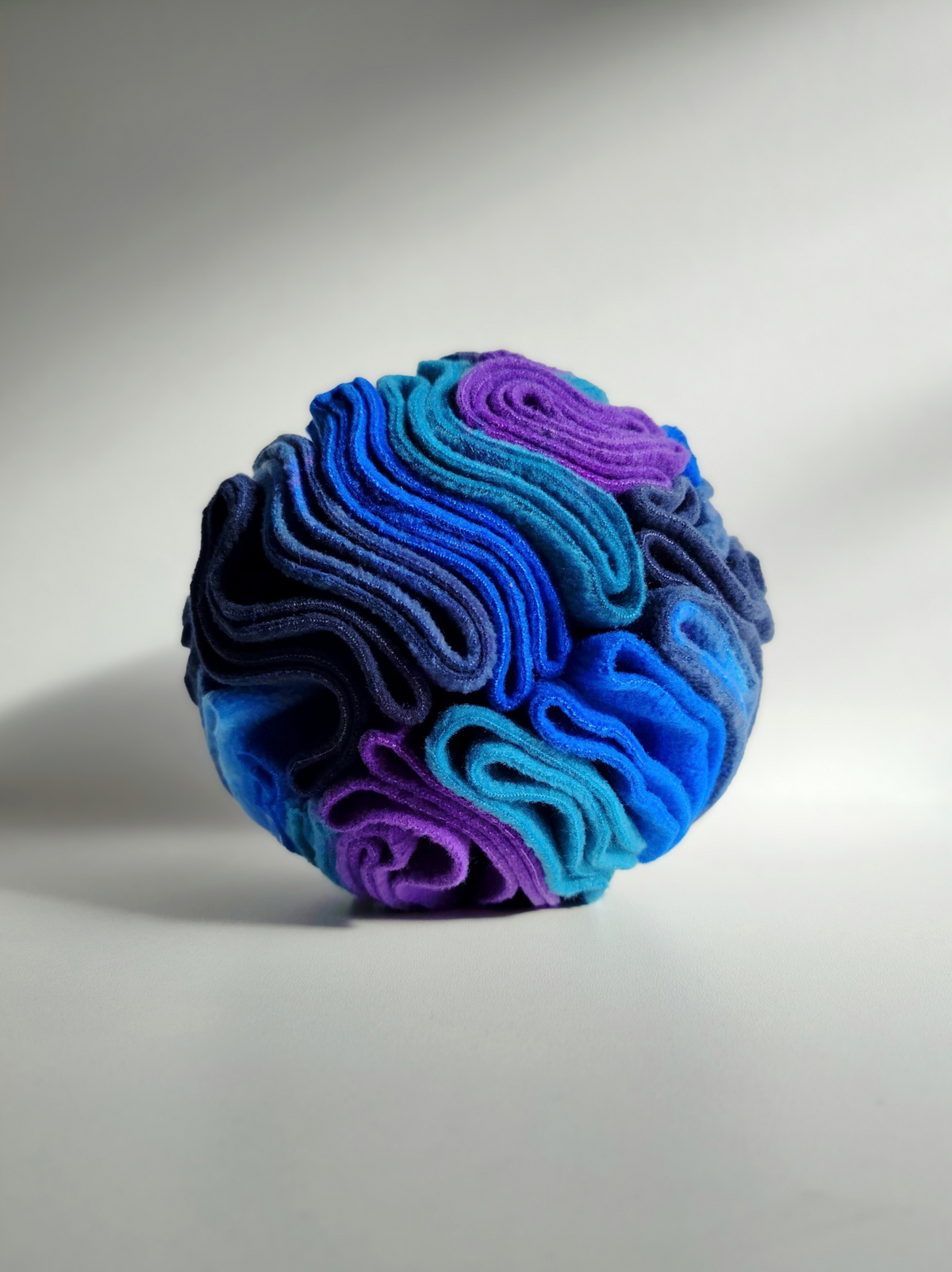 Close-up of a Medium Nova Zeal Night Sky Snuffle Ball showing tightly layered fleece folds in navy, royal blue, teal and purple, photographed against a light background.
