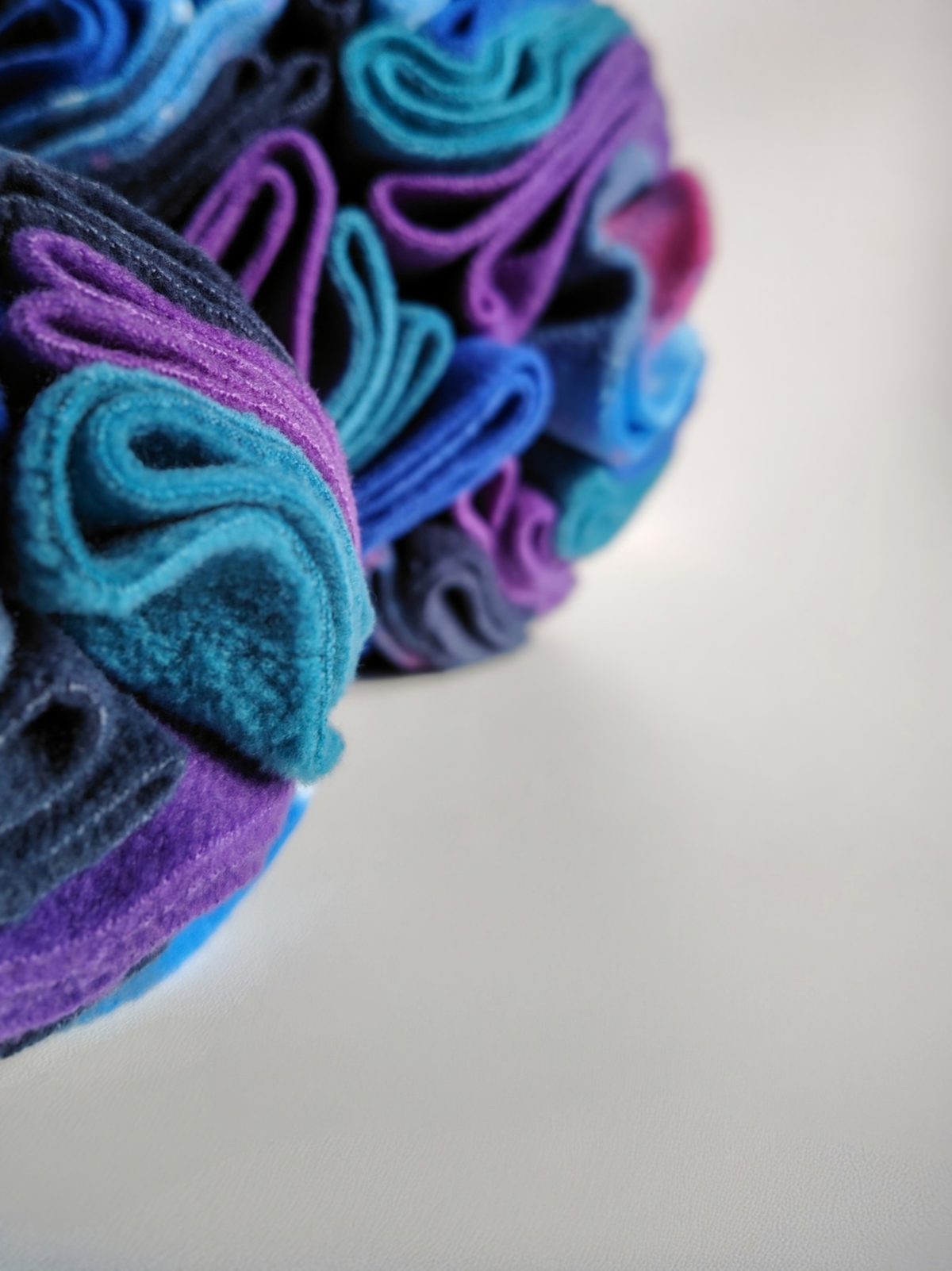 Close-up of Nova Zeal Night Sky Snuffle Balls, highlighting the soft, folded fleece in teal, purple, navy and blue, with a second ball softly blurred in the background.