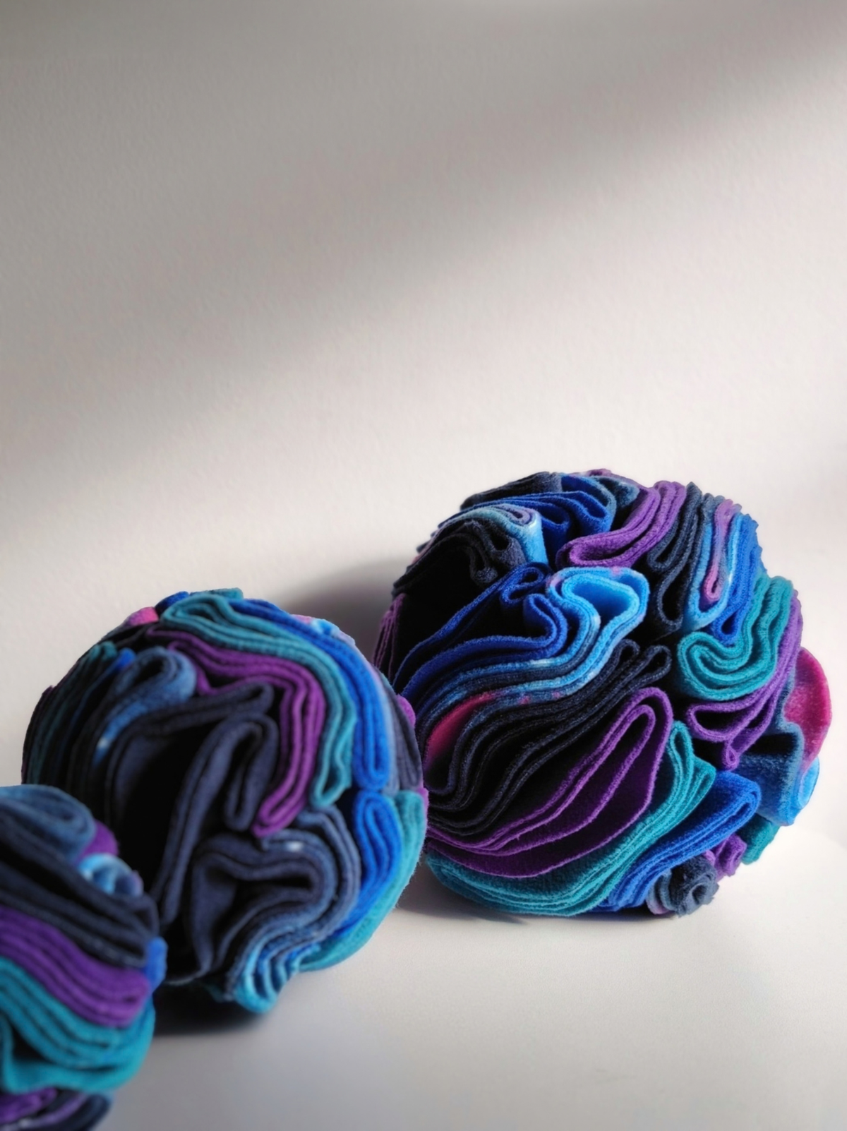 Three Nova Zeal Night Sky Snuffle Balls arranged together, showing different sizes and layers of folded fleece in navy, royal blue, teal, purple and galaxy print.