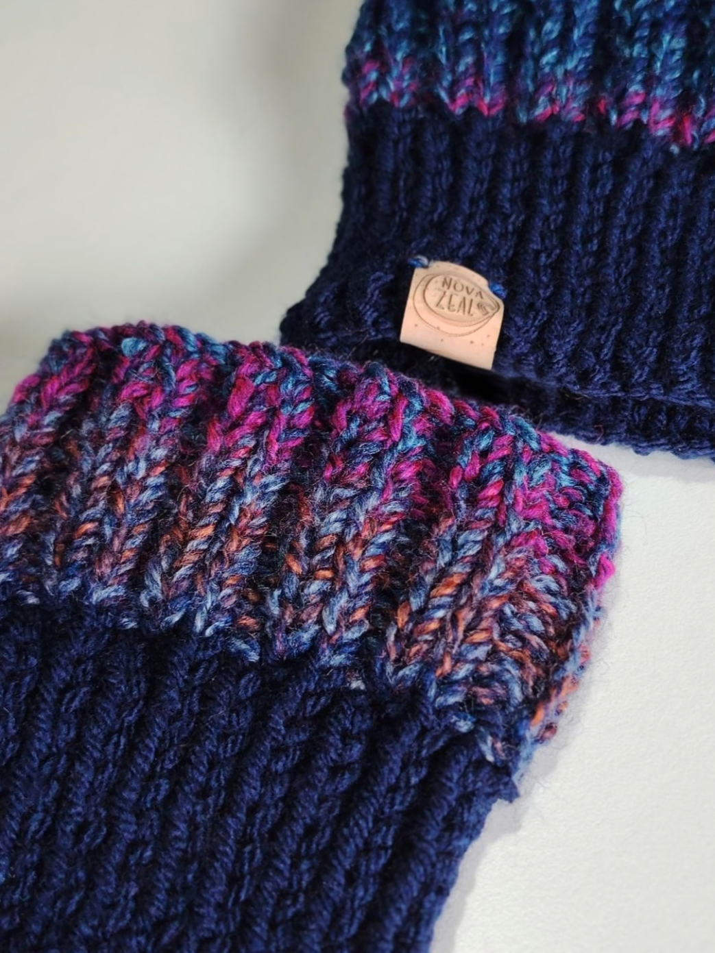 Close-up of two Nova Zeal Night Sky hand-knitted dog snoods in blue and purple yarn, showing the ribbed knit texture and cork labels.