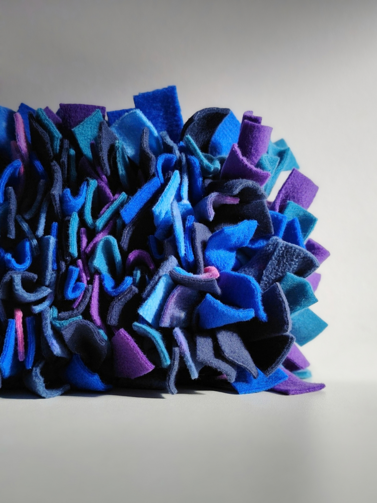 Close-up of the corner of Nova Zeal's Night Sky Snuffle Mat, highlighting the densely packed fleece strips in navy, royal blue, teal, purple and galaxy-patterned fleece against a light grey background.