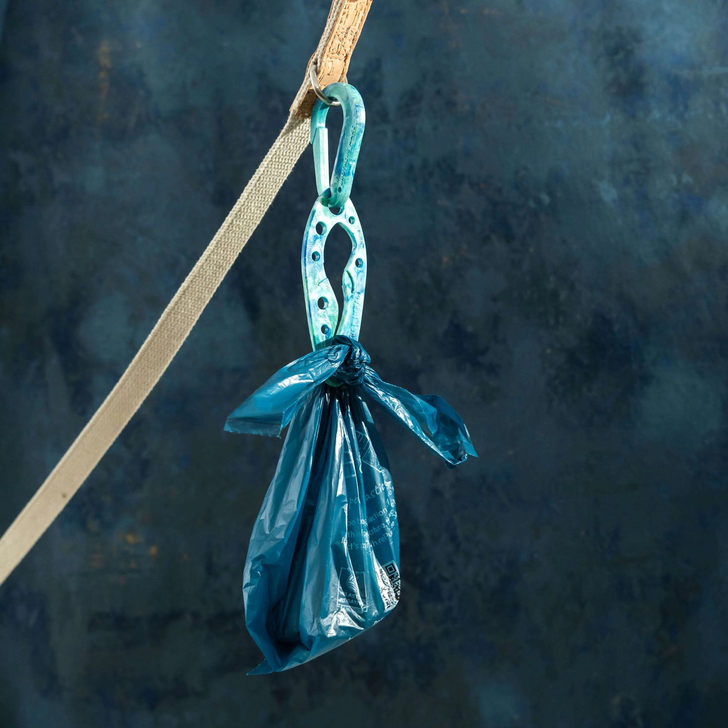 Blue PooPal attached to a dog lead, holding a tied blue poo bag against a textured blue background.