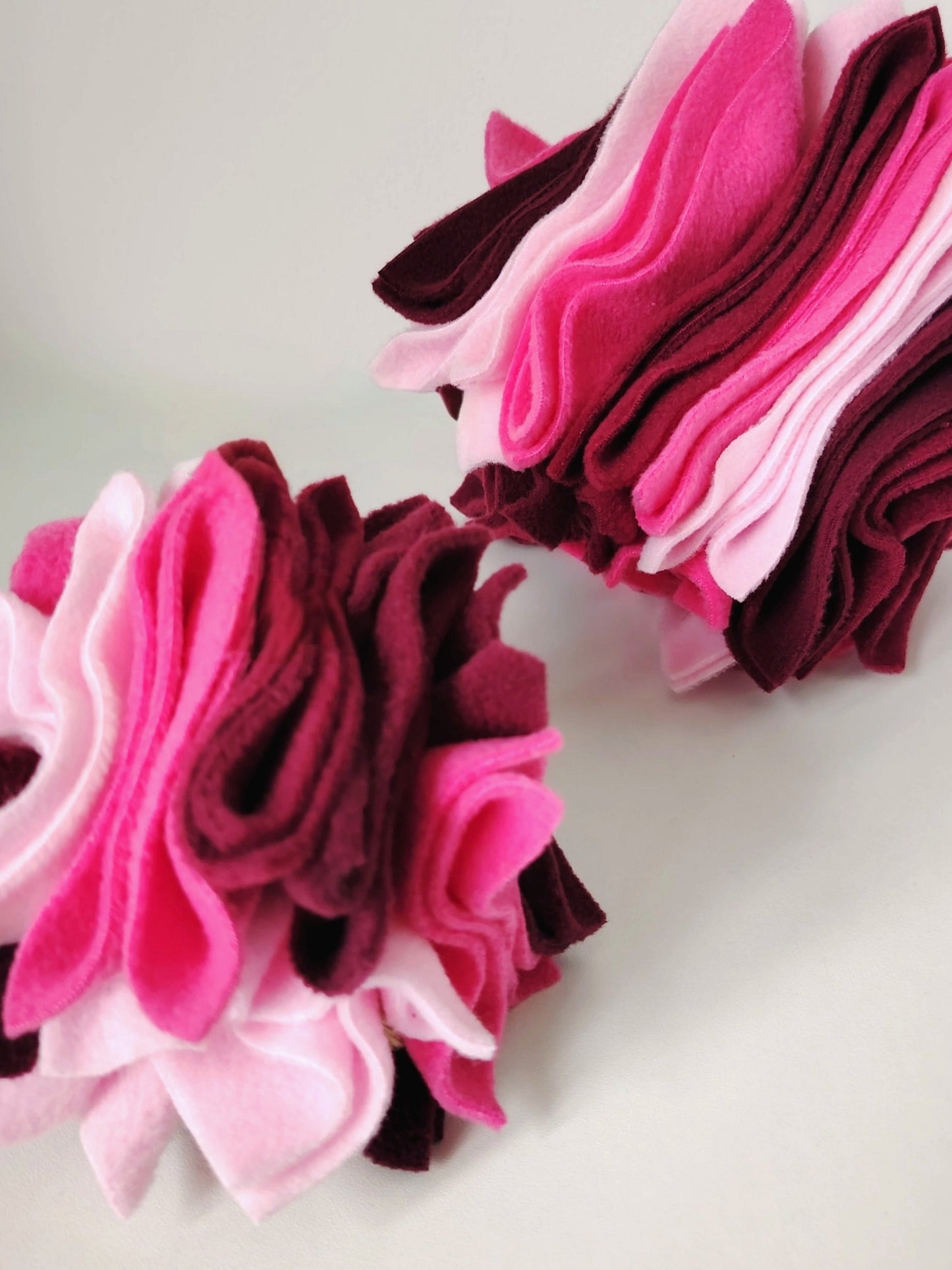 A small and large Nova Zeal Scruffle Balls in layered pink, pastel pink, plum and burgundy fleece.