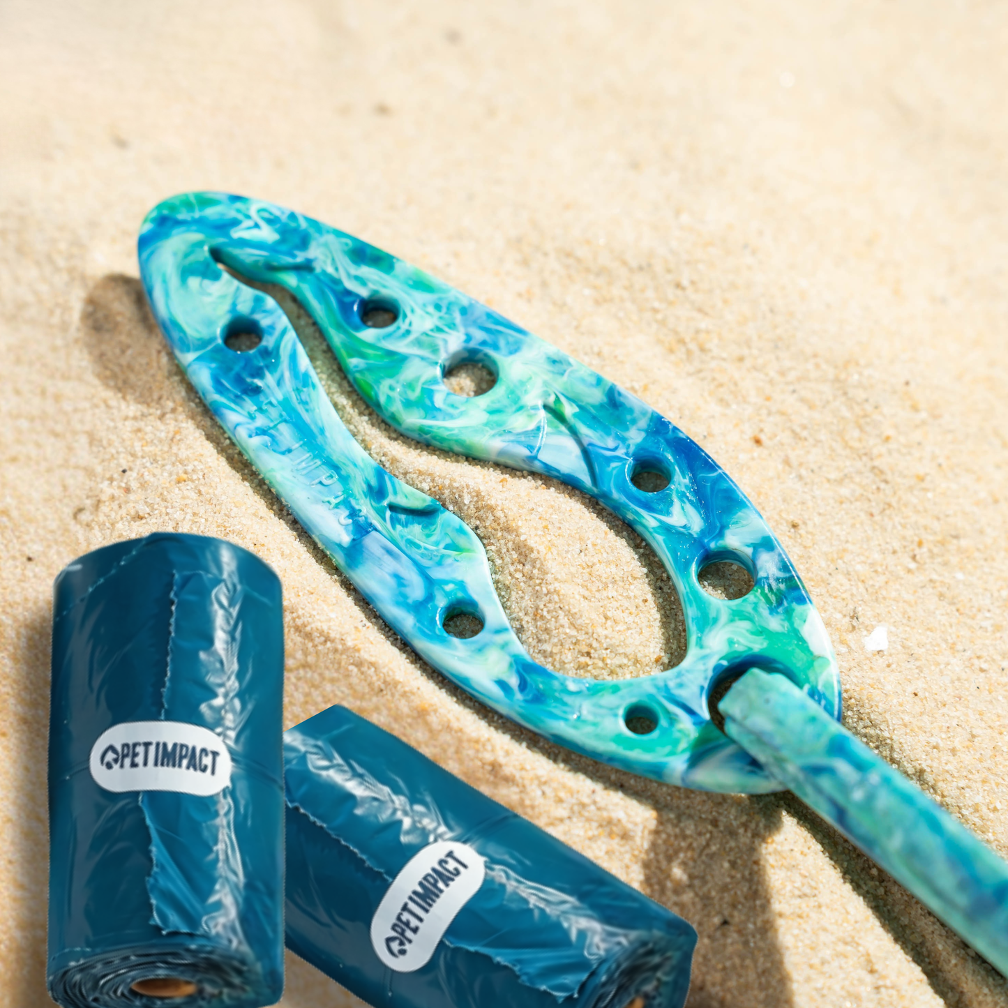 PooPal hands-free poo bag holder with two rolls of ReSEAcled poo bags on sand for convenient dog walks and outdoor adventures.
