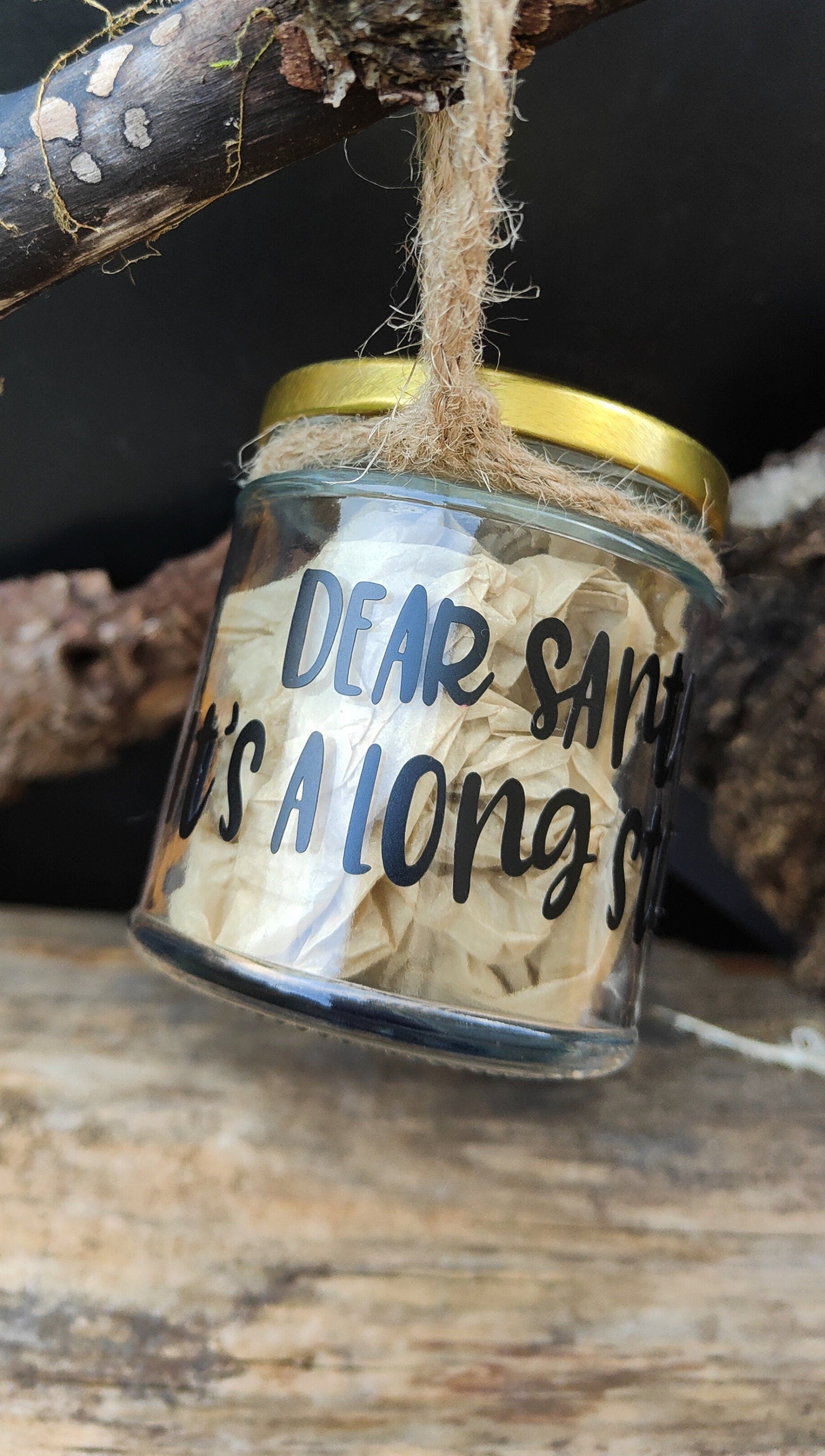 Glass treat jar with gold lid labeled 'Dear Santa, It's a long Story', hanging on a branch.