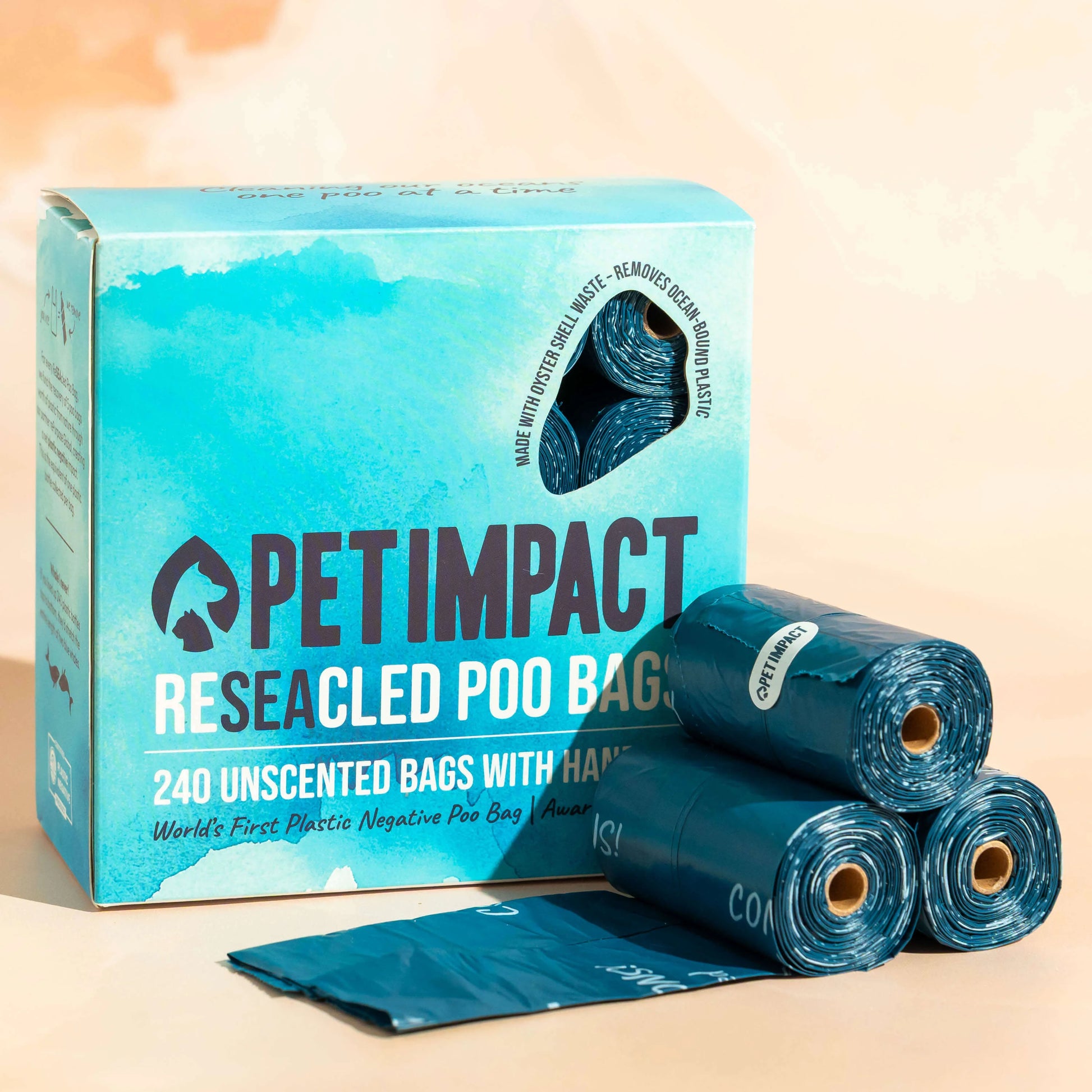 Box of Pet Impact ReSEAcled dog poo bags displayed with several blue rolls and one unfolded bag on a pale background.