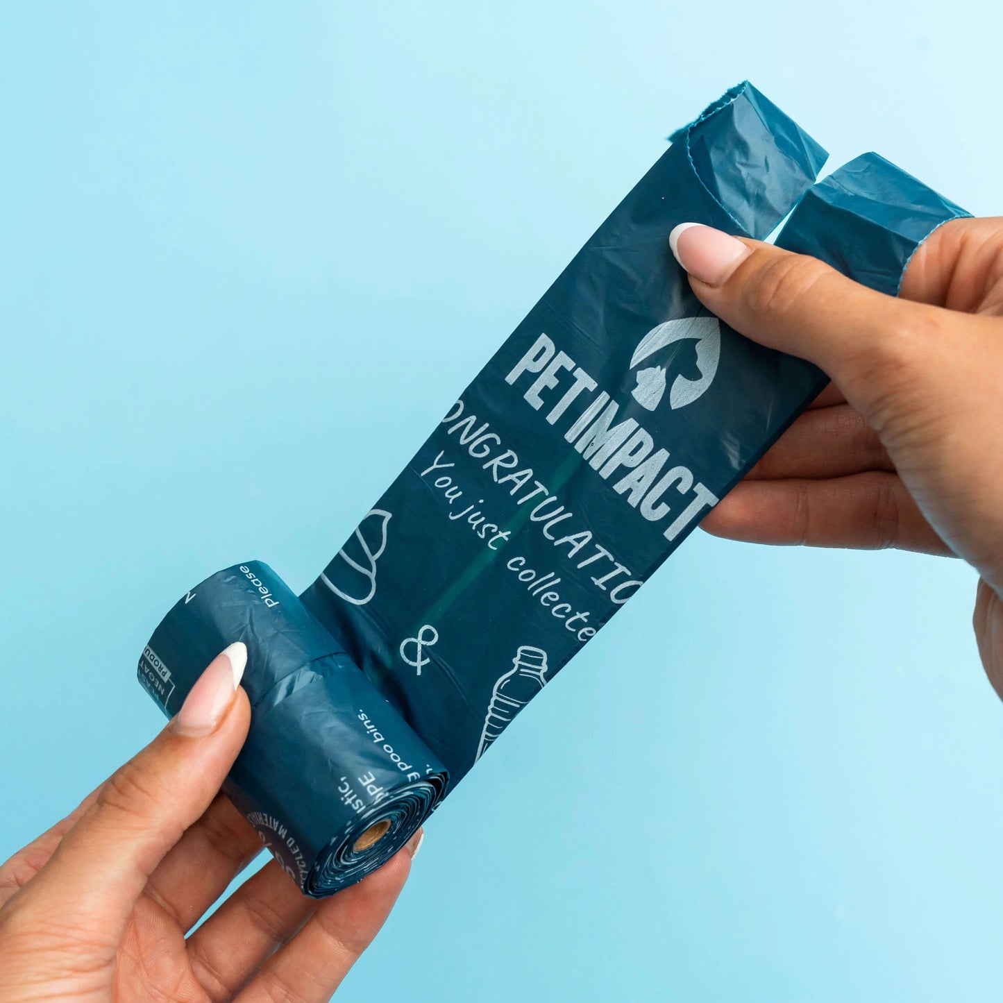 Hands unrolling a blue Pet Impact ReSEAcled dog poo bag, showing the printed message and easy-tear roll design.