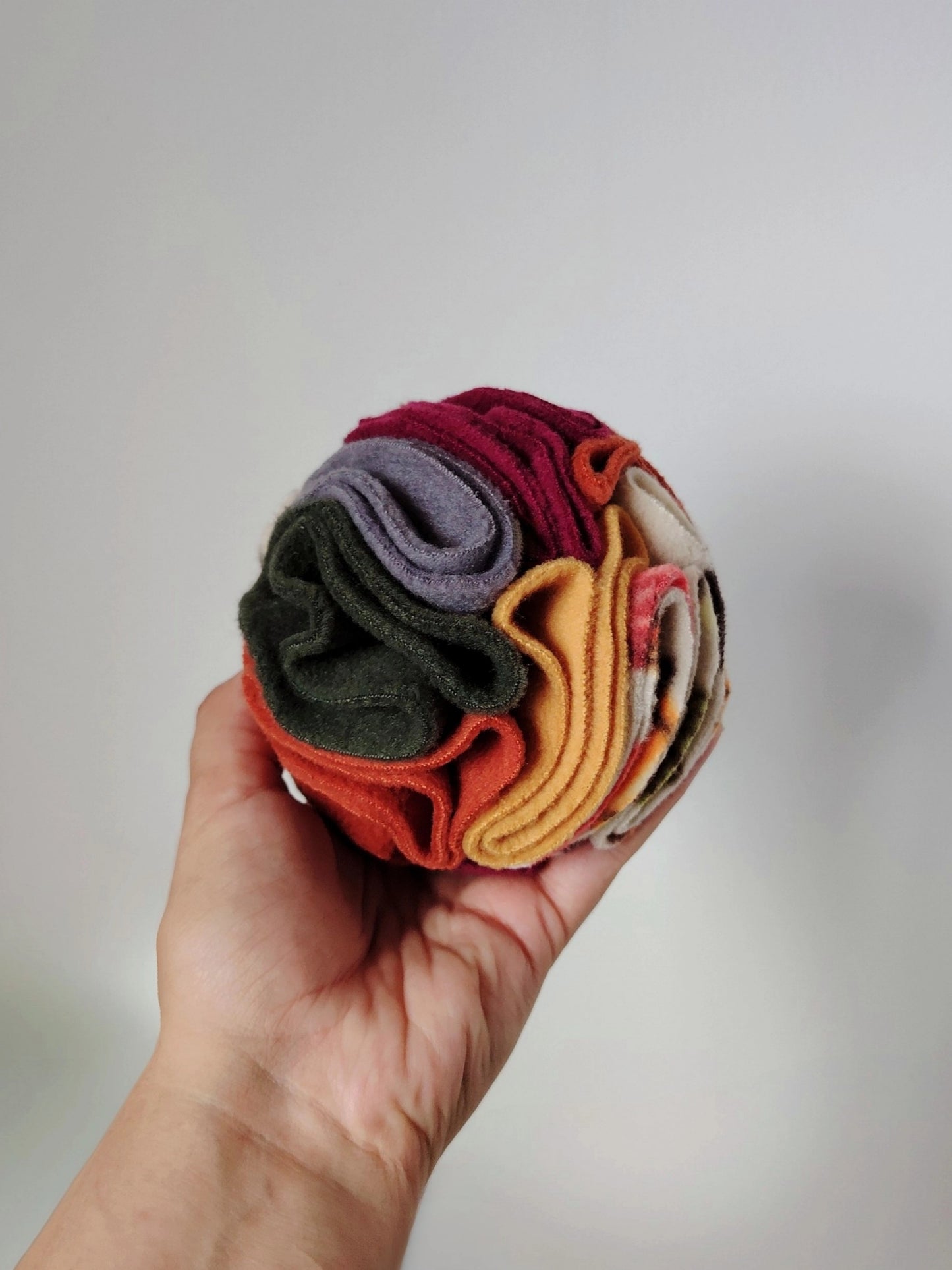 Small Autumn Snuffle Ball for dogs and small pets held in one hand to show its size and fleece folds.
