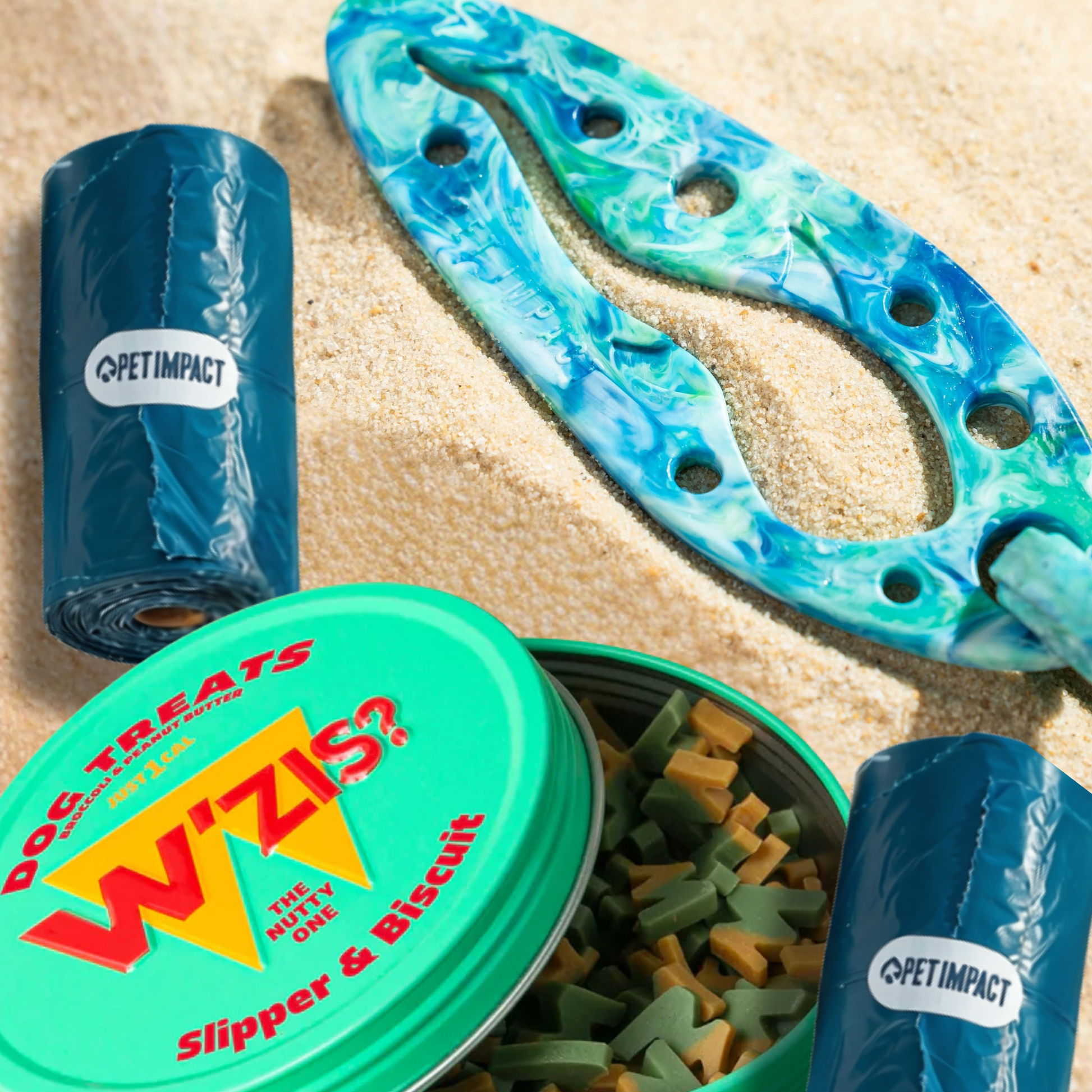 Travel Essentials Bundle featuring a PooPal hands-free poo bag holder, two rolls of ReSEAcled poo bags and a W'ZIS dog treat tin on a sandy background.