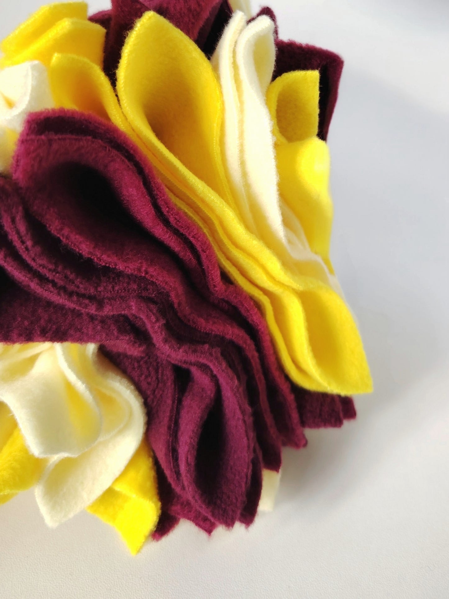 Close-up of a Nova Zeal Scruffle Ball showing layered yellow, lemon, plum and burgundy fleece folds.